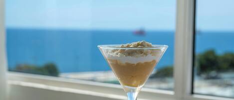 A martini glass with a dessert on a table by a window with a view of the ocean.