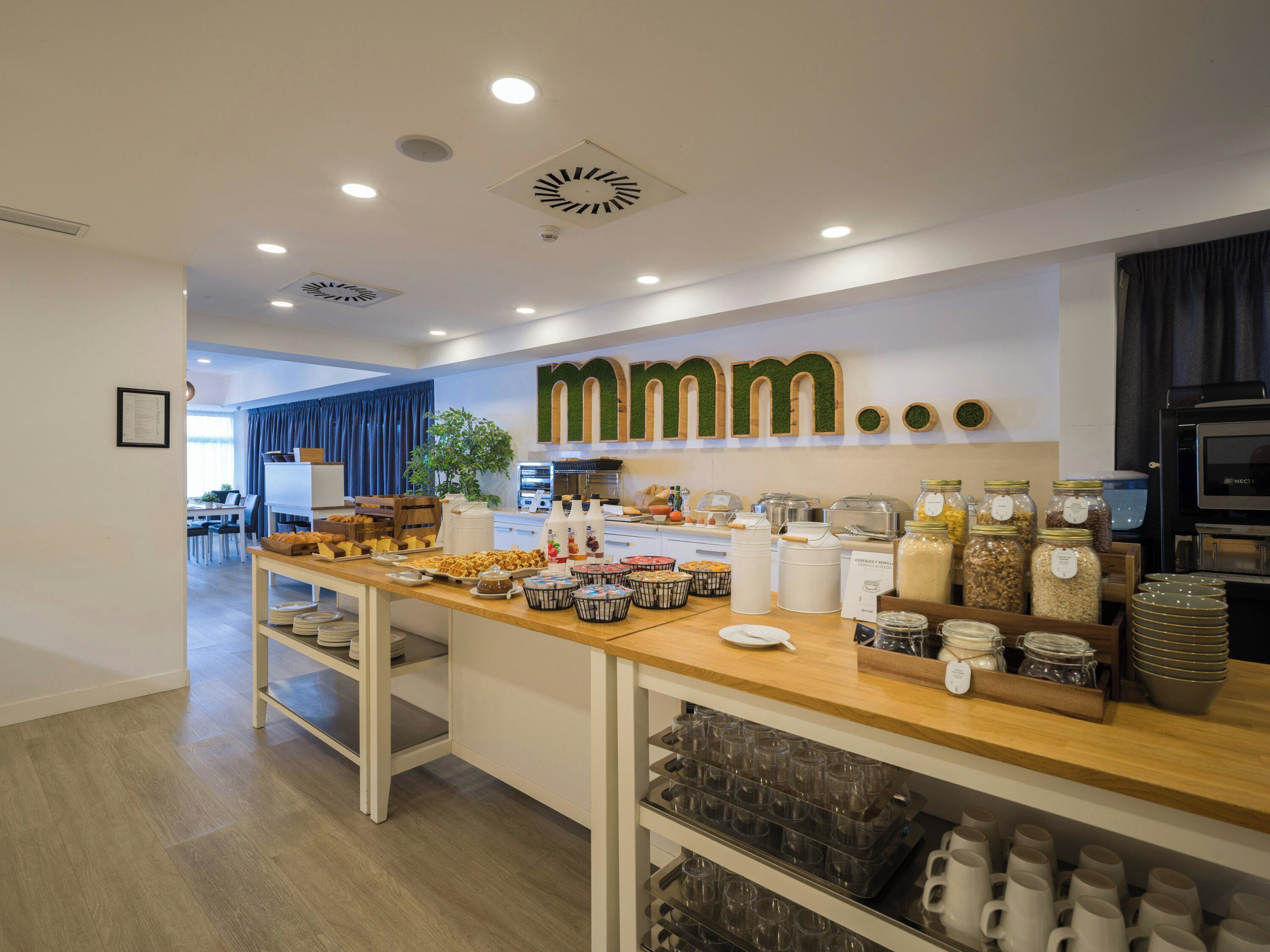 A breakfast buffet with various food items, a coffee station, and a kitchen area with a TV.
