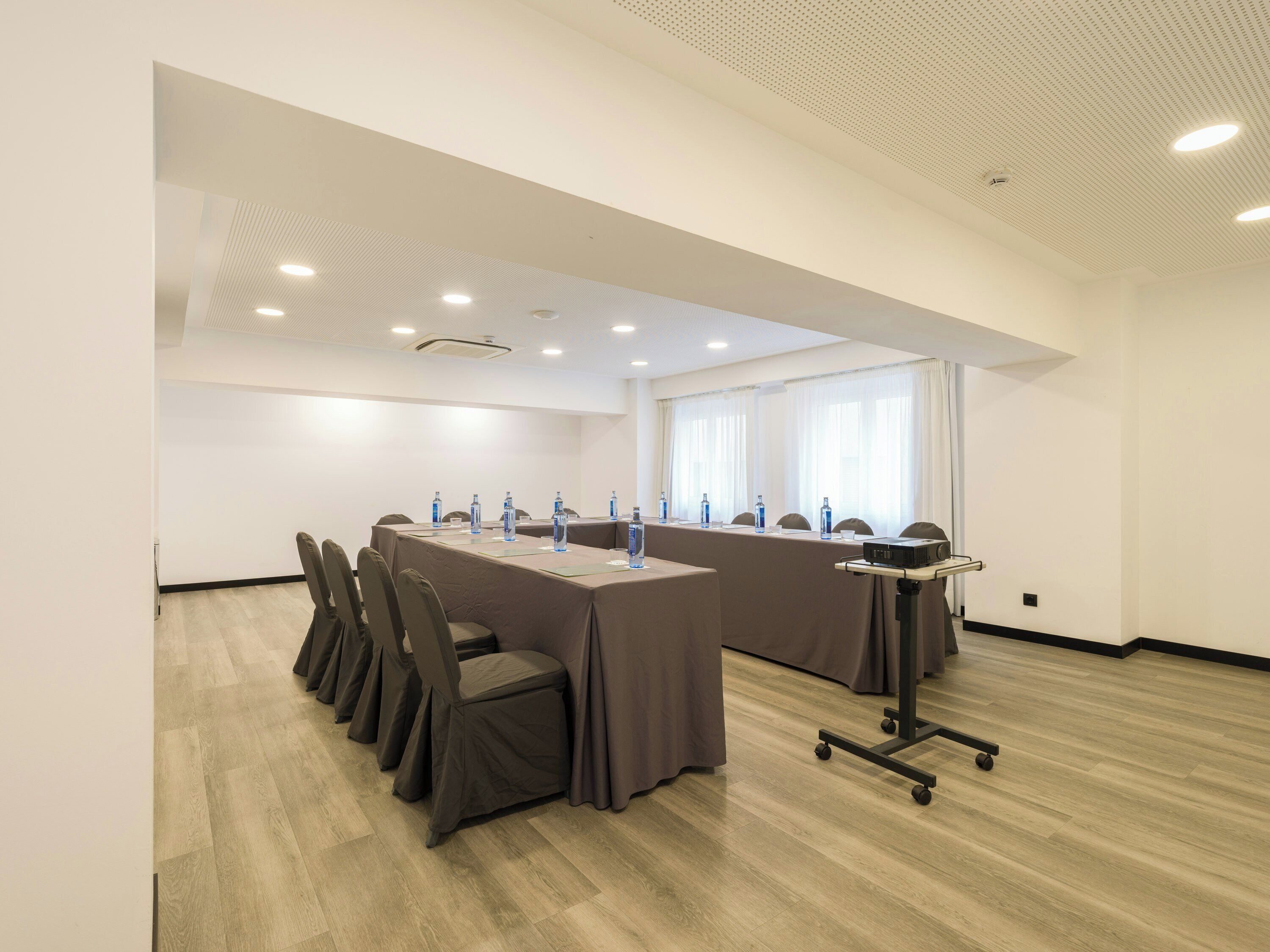 Un salón de conferencias con una larga mesa, sillas, botellas de agua, un proyector e iluminación empotrada en el techo.