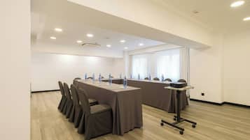 Un salón de conferencias con una larga mesa, sillas, botellas de agua, un proyector e iluminación empotrada en el techo.