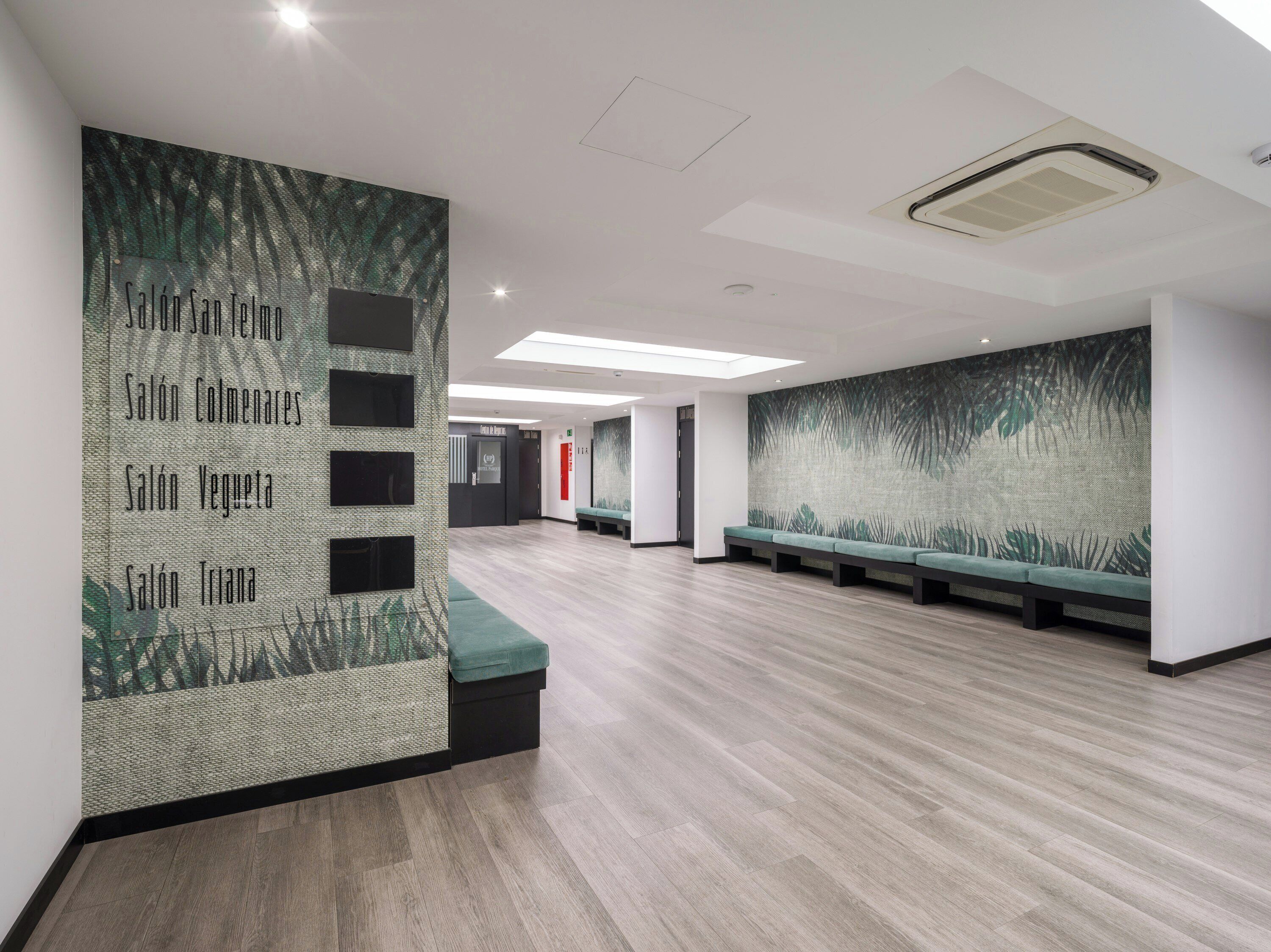 Una hall d'albergo con una reception, un'area salotto con panche e un grande murale.
