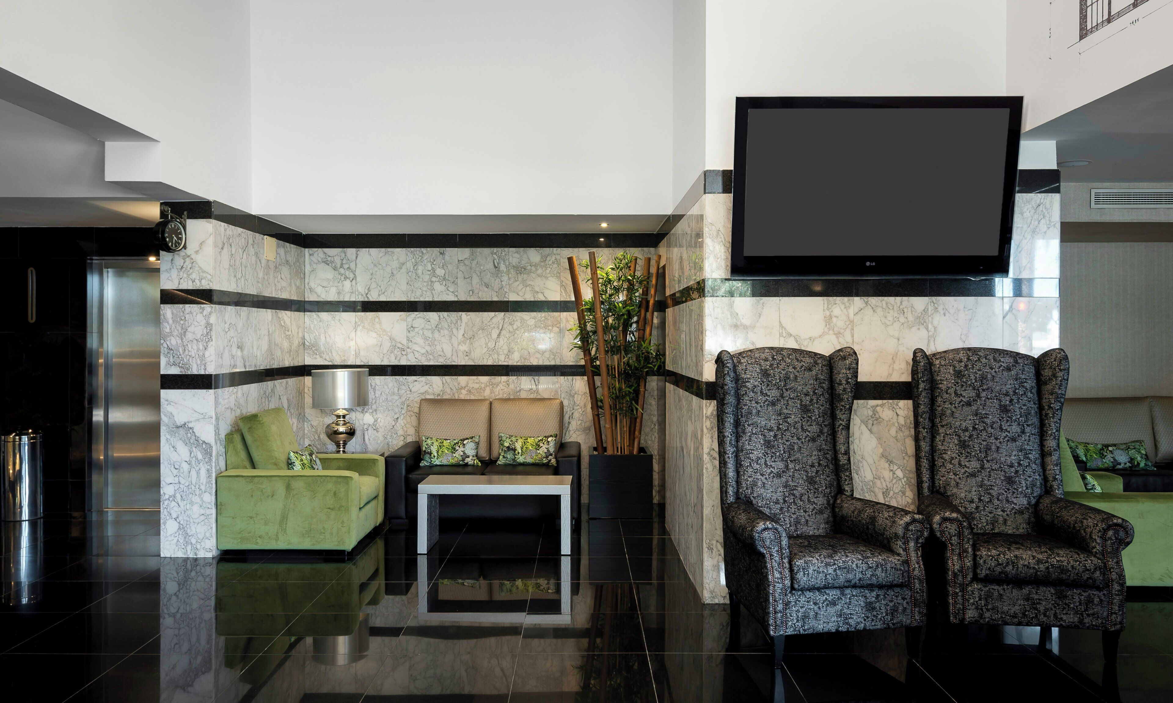 Una hall moderna con un divano, poltrone, un tavolino da caffè, una TV a schermo piatto e una pianta decorativa.