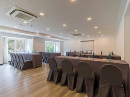 Ein Konferenzraum mit einem langen Tisch, Stühlen, einer Projektionsleinwand und einem großen Fenster.