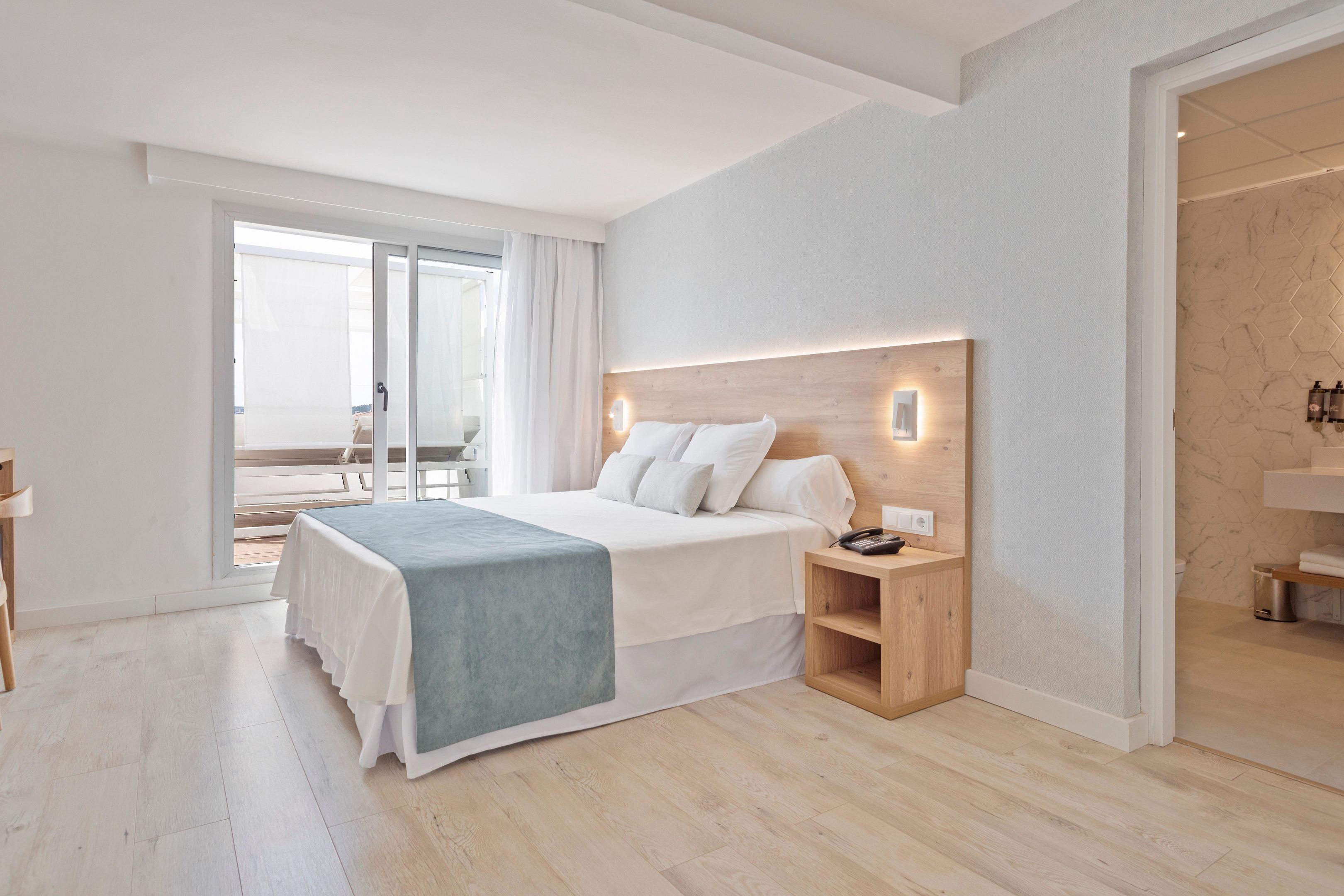 Een moderne slaapkamer met een groot bed, een nachtkastje en uitzicht op een balkon.