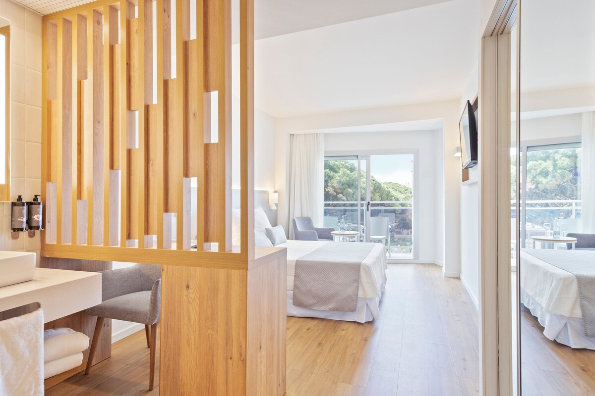 A modern hotel room with a wooden partition, a bed, a seating area, and a balcony with a view.