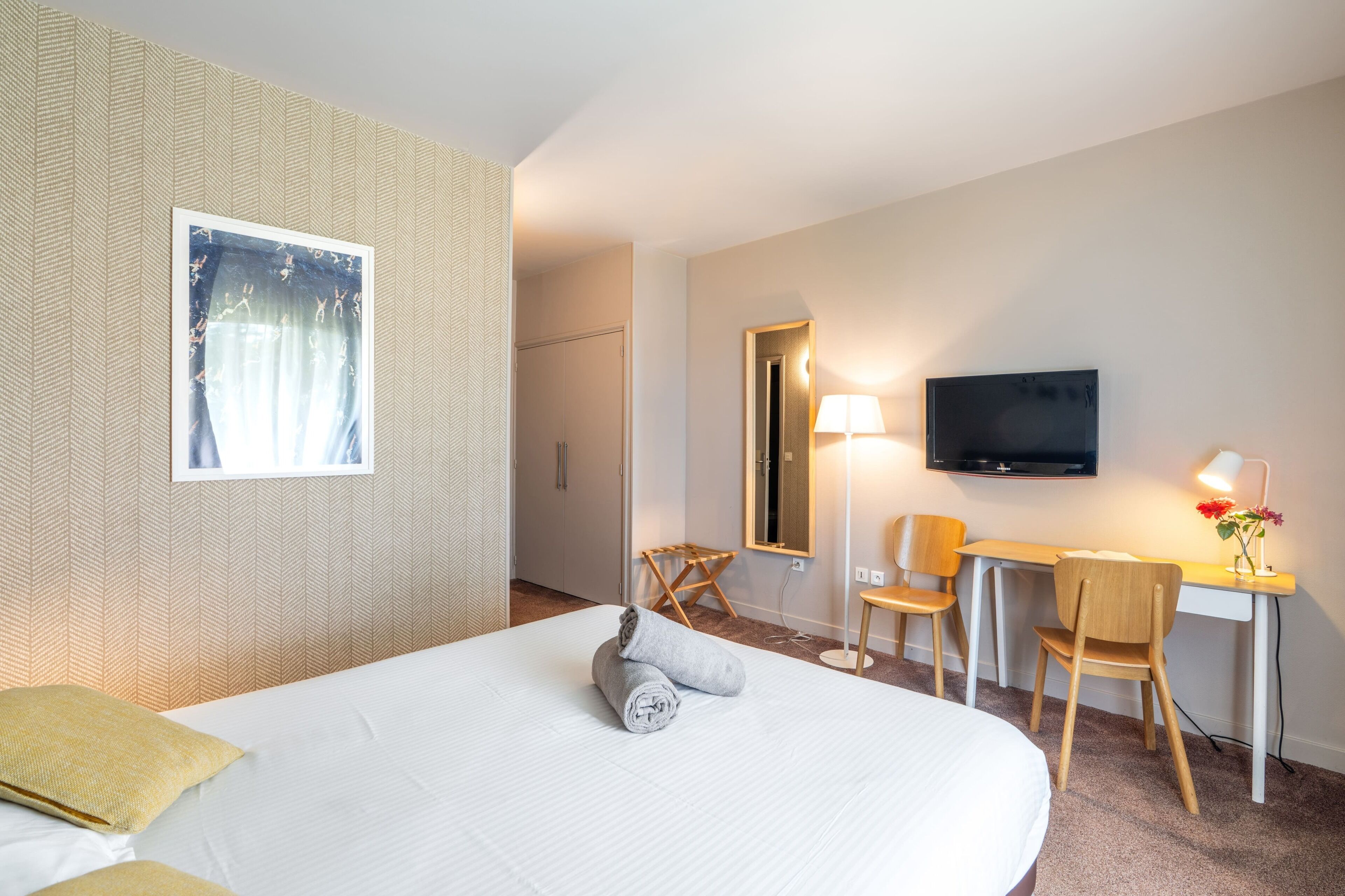 A hotel room with a bed, a desk, a chair, a television, and a window with curtains.