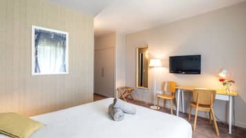 Une chambre d’hôtel équipée d’un lit, d’un bureau, d’une chaise, d’une télévision et d’une fenêtre avec des rideaux.