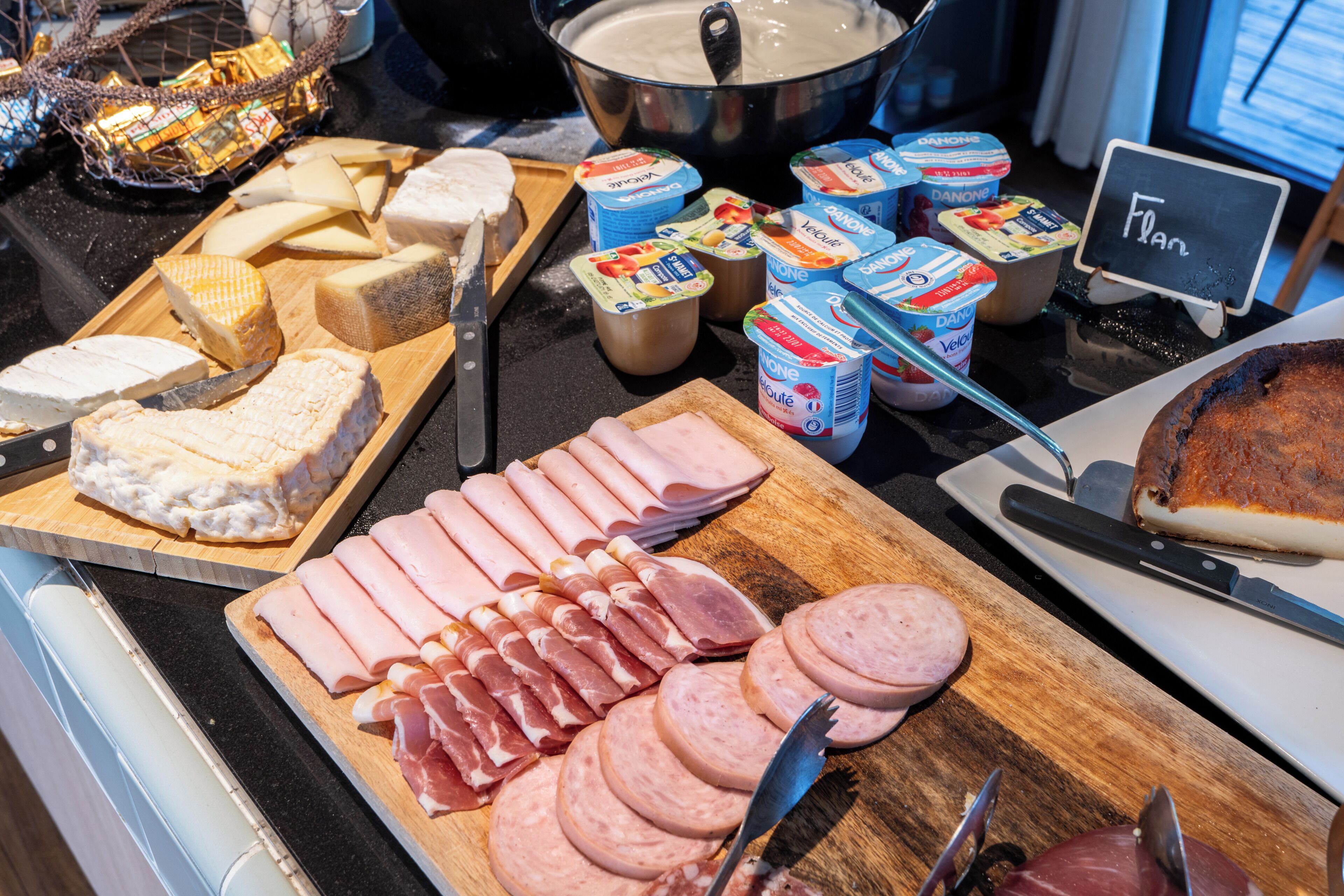 A buffet table with various cheeses, meats, and dairy products.