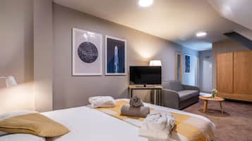 A hotel room with a bed, a TV, a sofa, a wooden wardrobe, and two framed pictures on the wall.