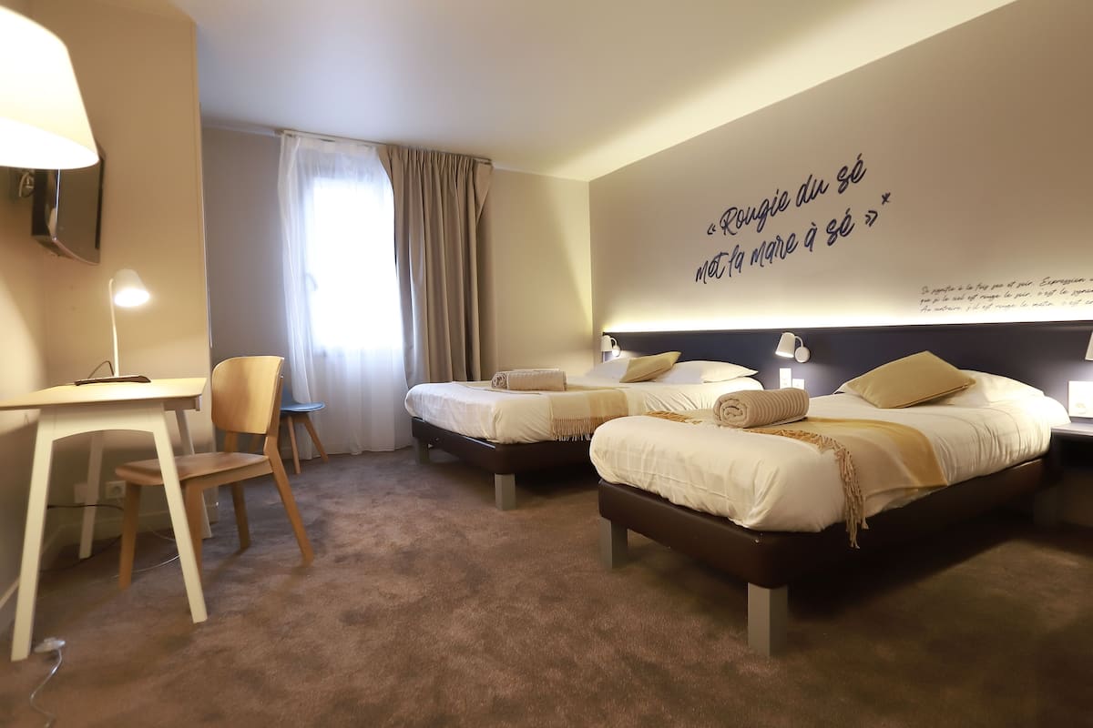 A hotel room with two beds, a desk, a chair, and a wall with a quote.