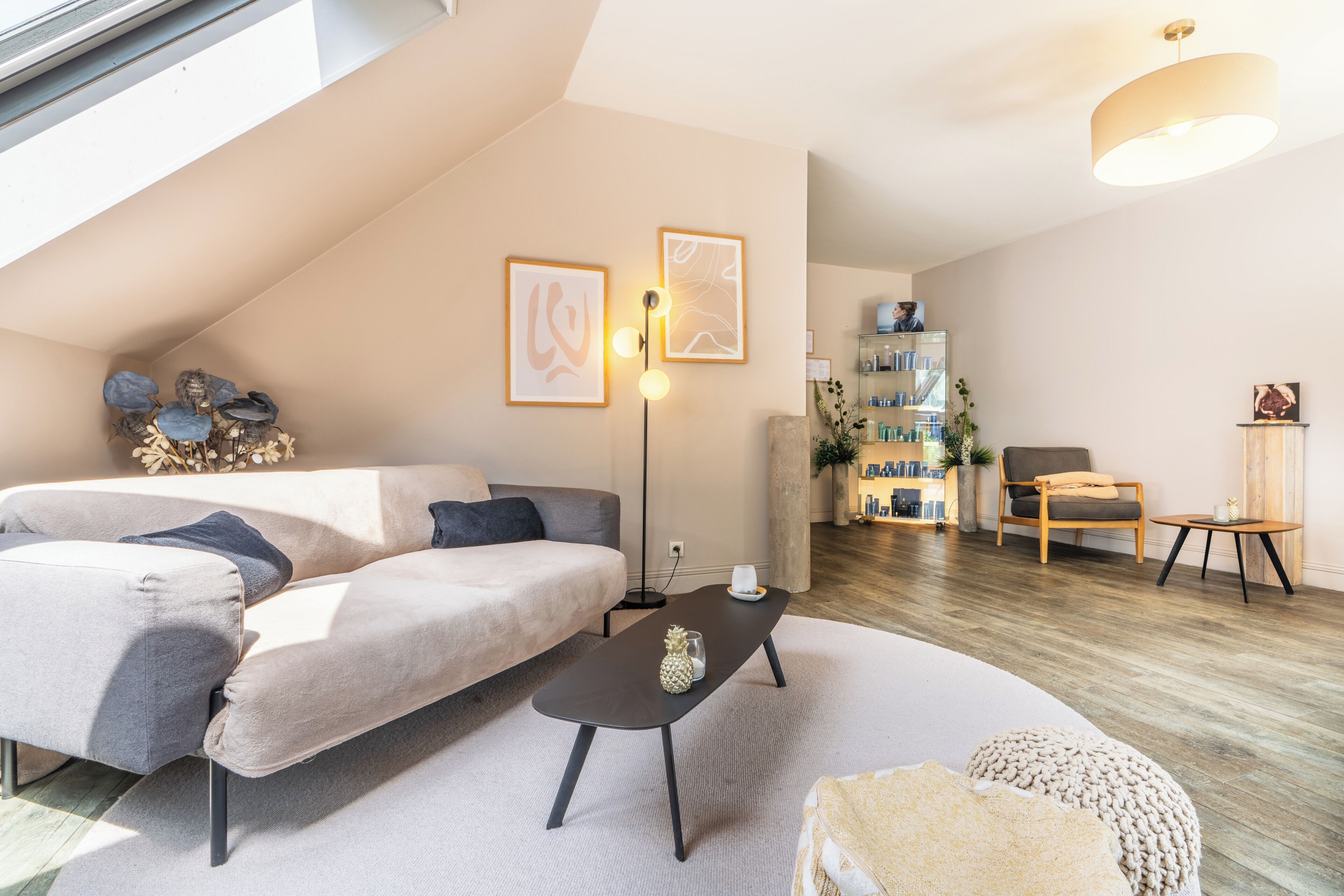 A modern living room with a sectional sofa, a coffee table, and a small side table. There is a bookshelf with decorative items and a plant.