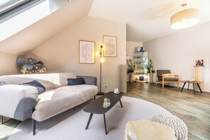 A modern living room with a sectional sofa, a coffee table, and a small side table. There is a bookshelf with decorative items and a plant. - Antares & Spa Honfleur (La Riviere-Saint-Sauveur)