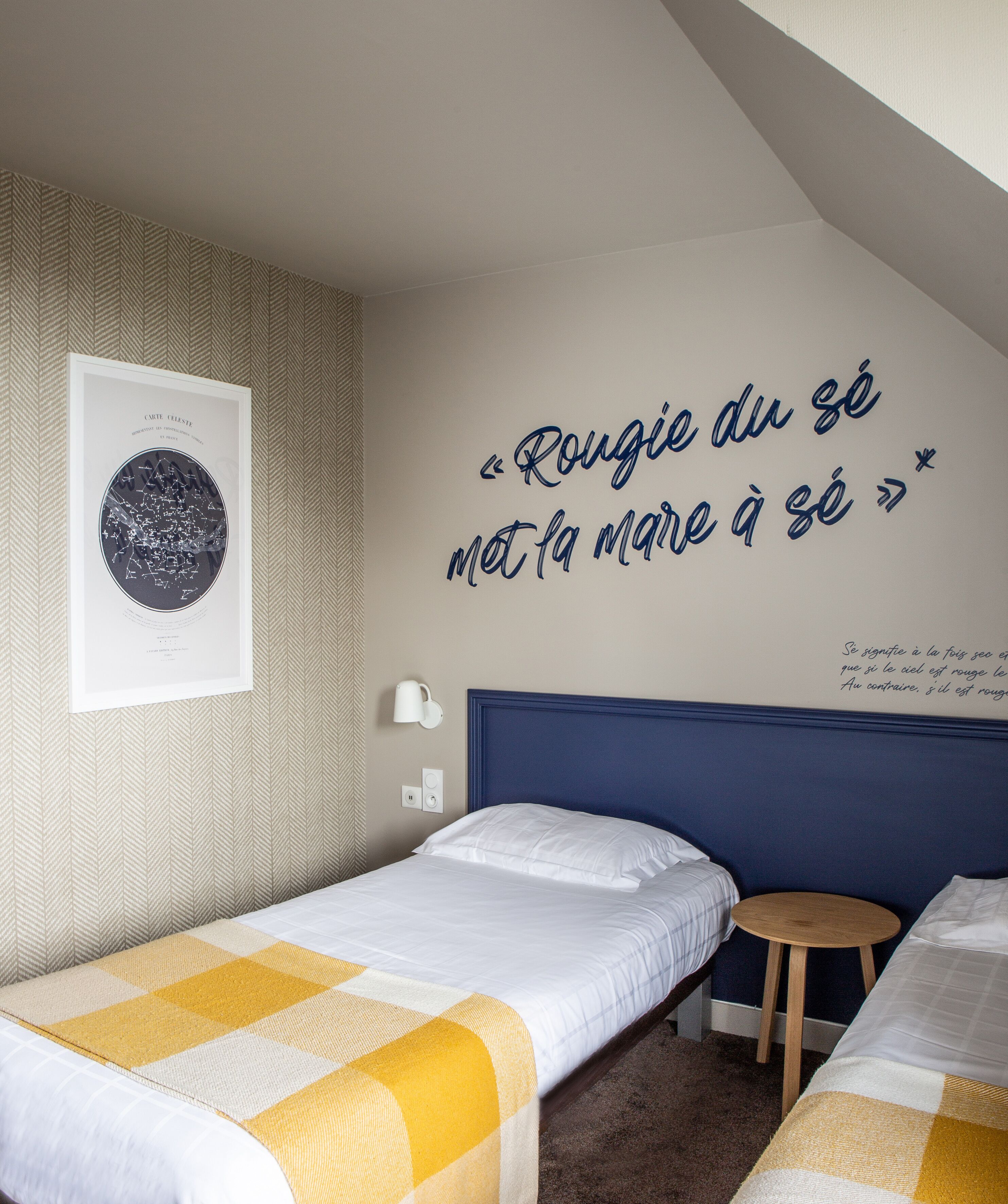 A hotel room with two single beds, a wall-mounted poster, and a small bedside table.