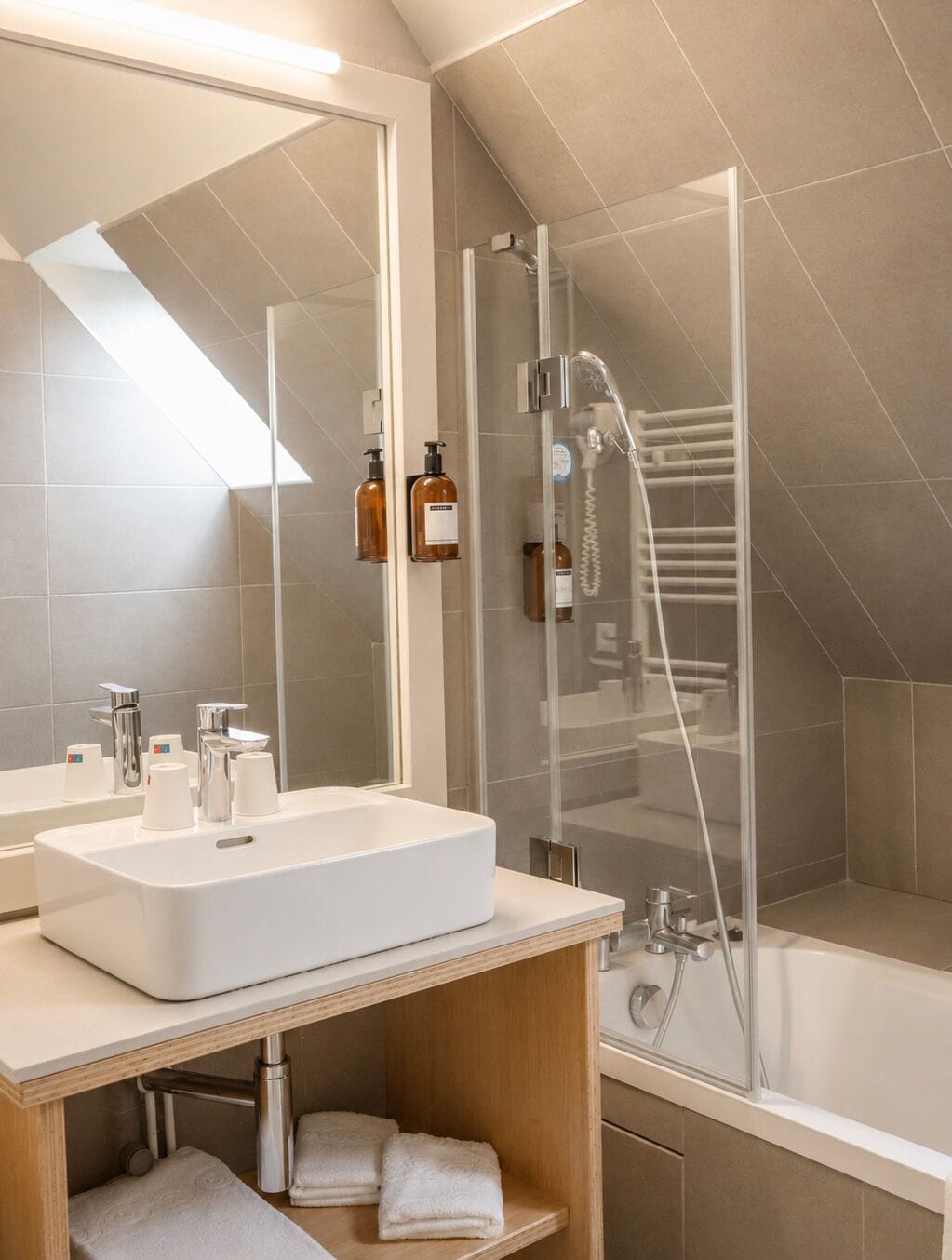 A modern bathroom with a large mirror, a white sink, a glass-enclosed shower, and a bathtub.