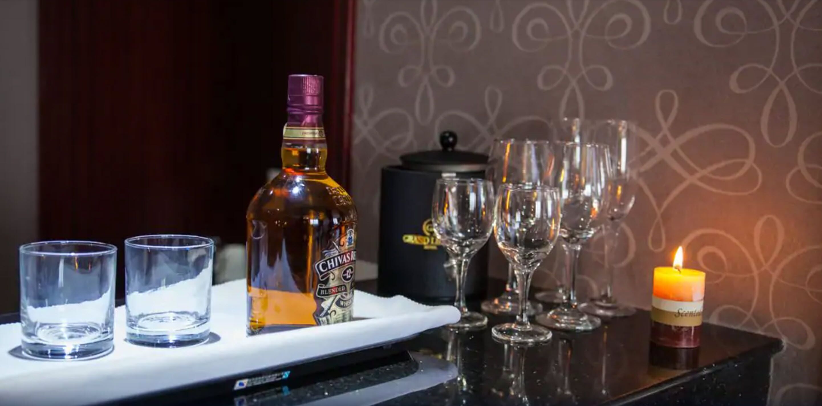 Un área de bar con una botella de Chivas, vasos y una vela.