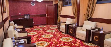A hotel room with a red carpet, two sofas, a small table, and a cabinet.