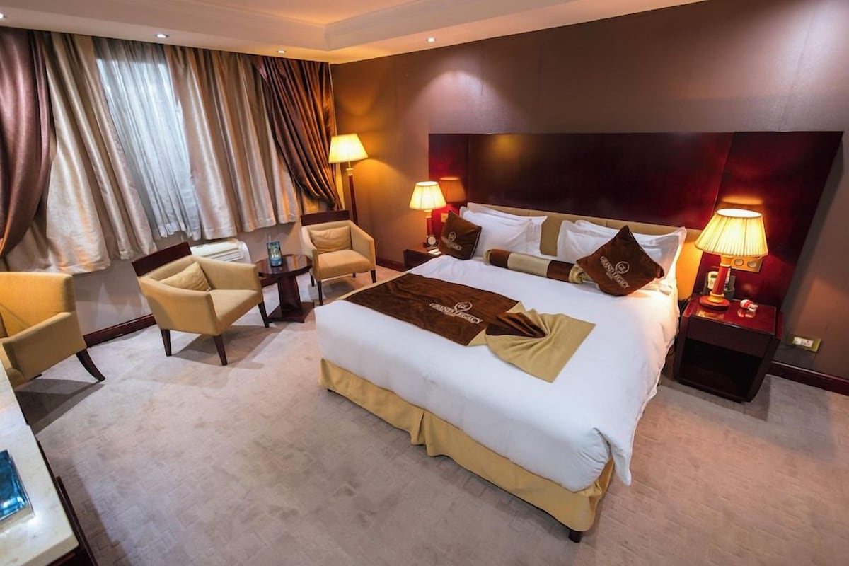 A hotel room with a large bed, two bedside tables with lamps, a chair, and a desk.