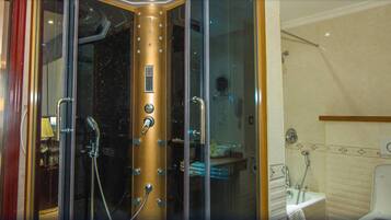 A glass-enclosed shower with a gold-colored control panel, a visible towel rack, and a bathroom with a toilet and sink.