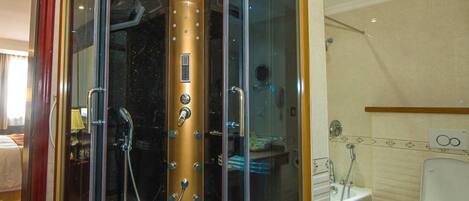 Doccia vetrata con pannello comandi dorato, porta asciugamani a vista e bagno con WC e lavandino.