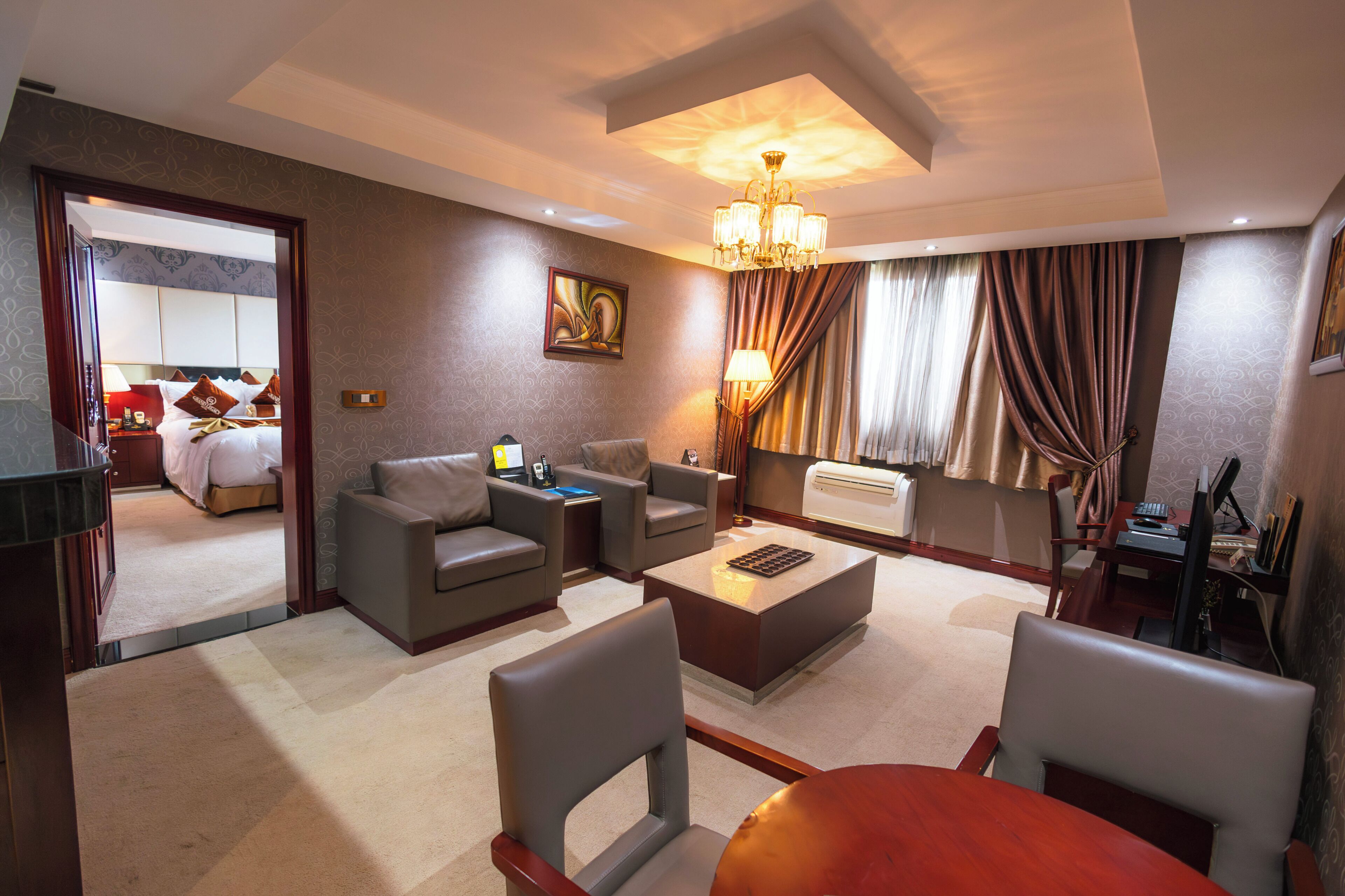 A hotel room with a living area, a dining table, a sofa, a coffee table, a TV, and a painting on the wall.