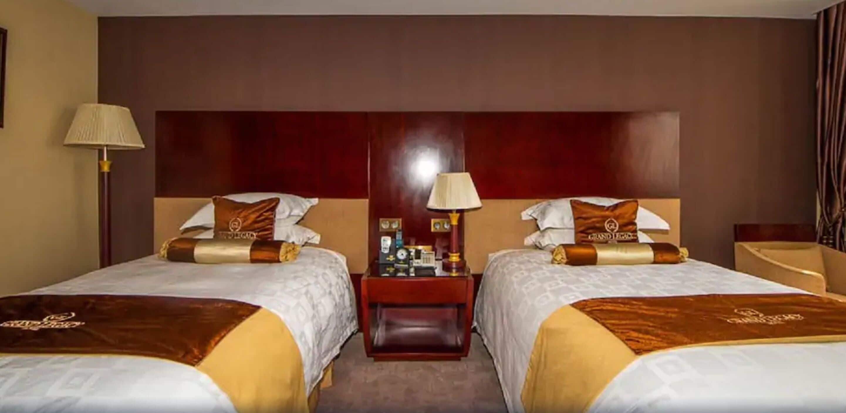 Ein Hotelzimmer mit zwei Betten, jeweils mit Kopfstütze, Nachttischen, Lampen und Dekokissen.