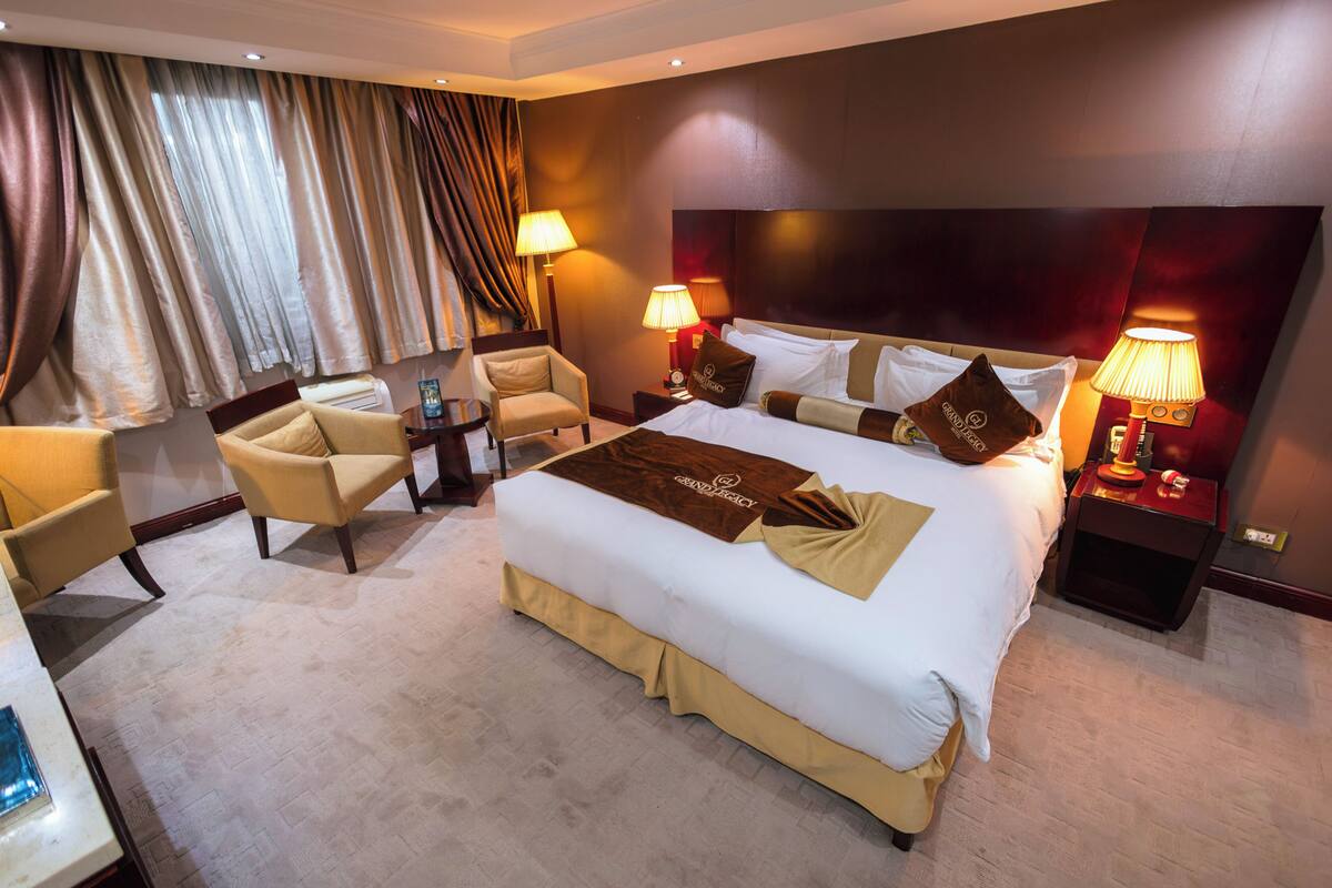 A hotel room with a large bed, two bedside tables with lamps, a chair, and a desk.