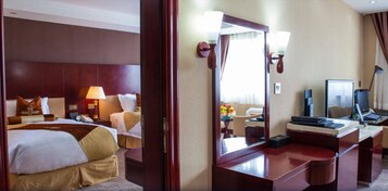 Habitación de hotel con dos camas, un escritorio con computadora, un espejo y un baño visible a través de una puerta.