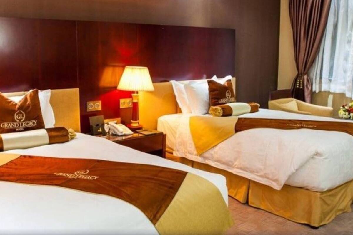 A hotel room with two beds, a nightstand with a lamp, a chair, and a desk with a telephone.