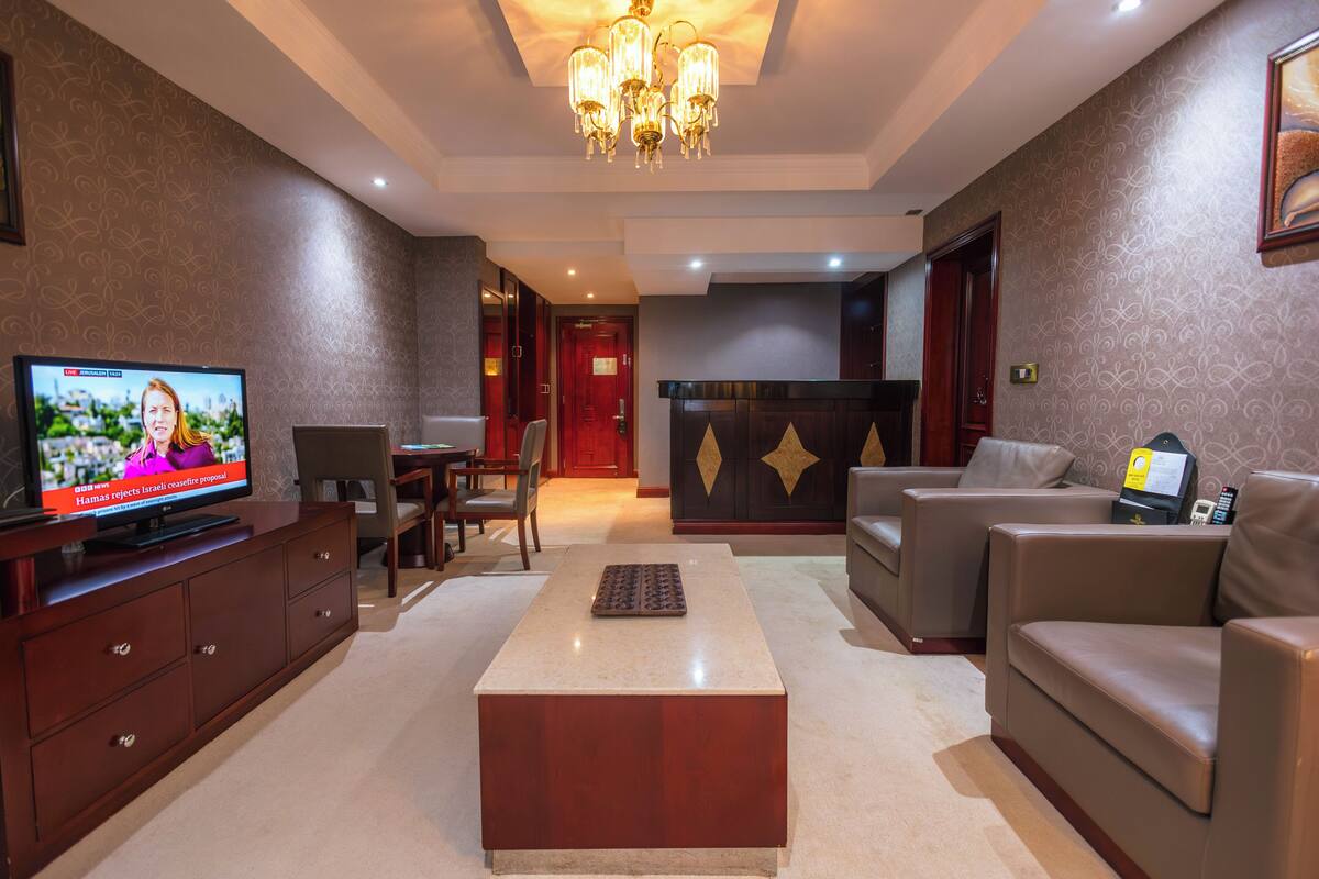 A hotel lobby with a television, a coffee table, sofas, a desk, and a chandelier.