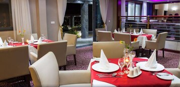 Un restaurante con mesas dispuestas para comer, con mantel rojo, servilletas blancas y velas.