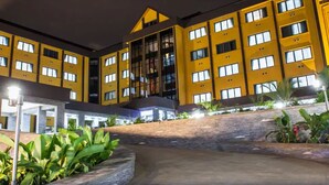 Un hotel de varios pisos con fachada amarilla, iluminación exterior y una zona ajardinada con plantas.