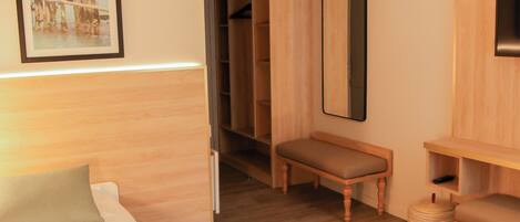 Quarto de hotel com cama, um banco, espelho, guarda-roupa e um quadro emoldurado na parede.
