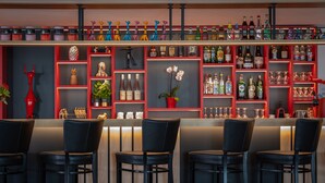 A bar area with multiple shelves of bottles and glasses, black bar stools, and a red decorative shelf with various items. - Le M Hôtel & Spa Honfleur (Honfleur)