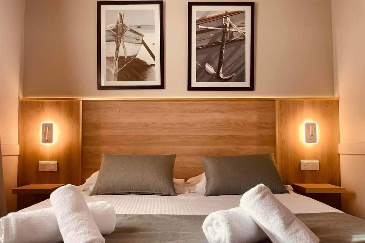 Ein Hotelzimmer mit einem hölzernen Kopfteil, zwei gerahmten Bildern über dem Bett und zwei Nachttischlampen.