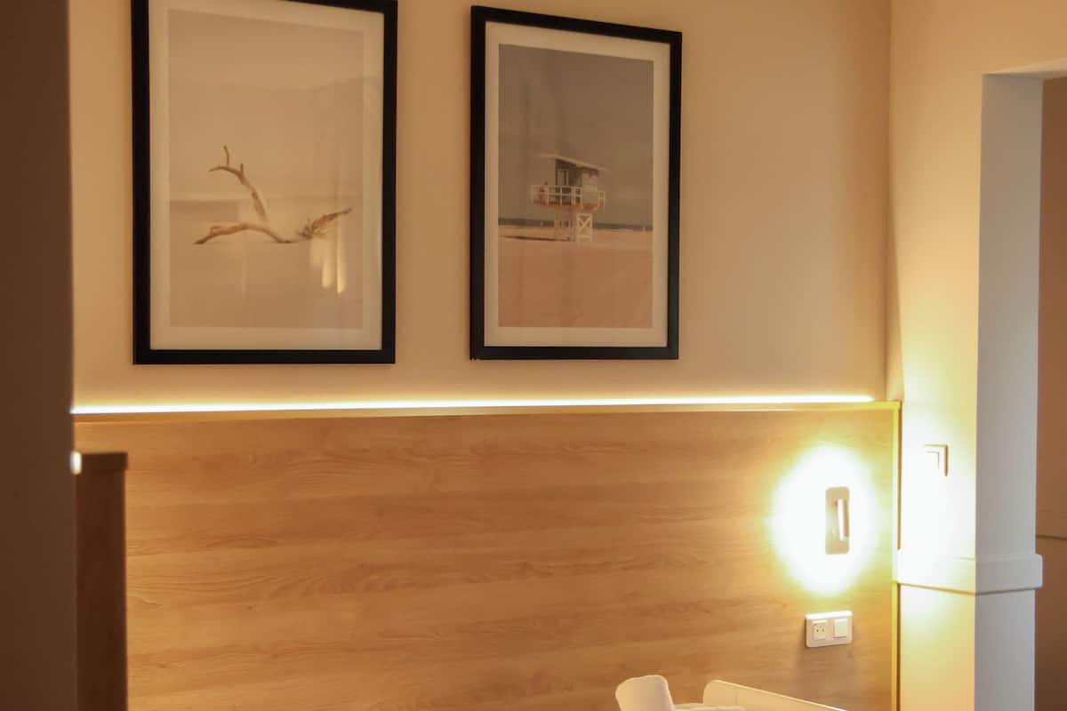 Ein Einzelbett mit Holzkopfstück, zwei gerahmte Bilder an der Wand und eine Nachttischlampe.