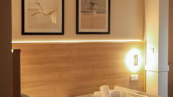 Un lit simple avec une tête de lit en bois, deux tableaux encadrés au mur et une lampe de chevet.