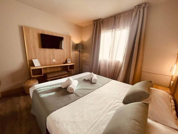 A hotel room with a bed, a TV mounted on the wall, a bedside table, and a window with curtains. - Le M Hôtel & Spa Honfleur (Honfleur)