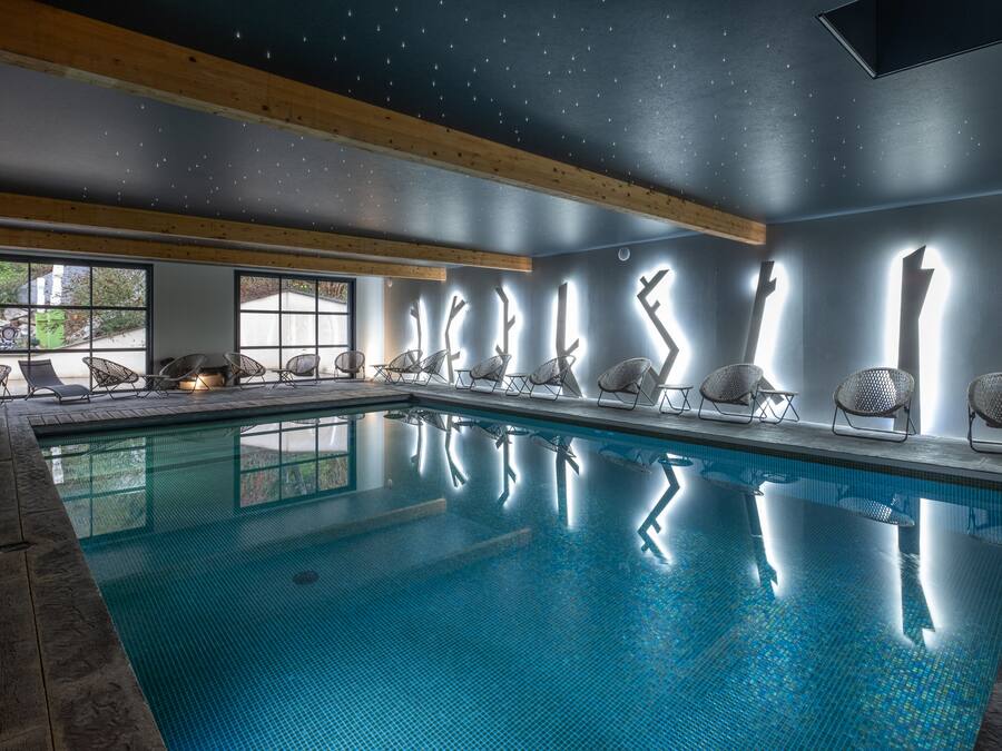 Una piscina con sillas a lo largo del borde, vigas de madera en el techo y vistas al exterior a través de amplias ventanas.