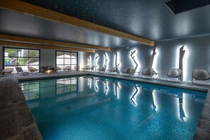 Una piscina con sillas a lo largo del borde, vigas de madera en el techo y vistas al exterior a través de amplias ventanas.