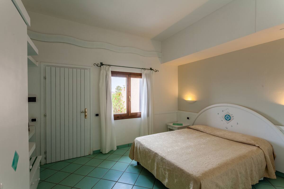 A bedroom with a bed, a window with curtains, a bedside table, and a door.