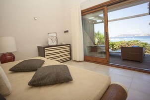 Un dormitorio con cama, cómoda, mesita de noche y vista al océano a través de un ventanal corredero.