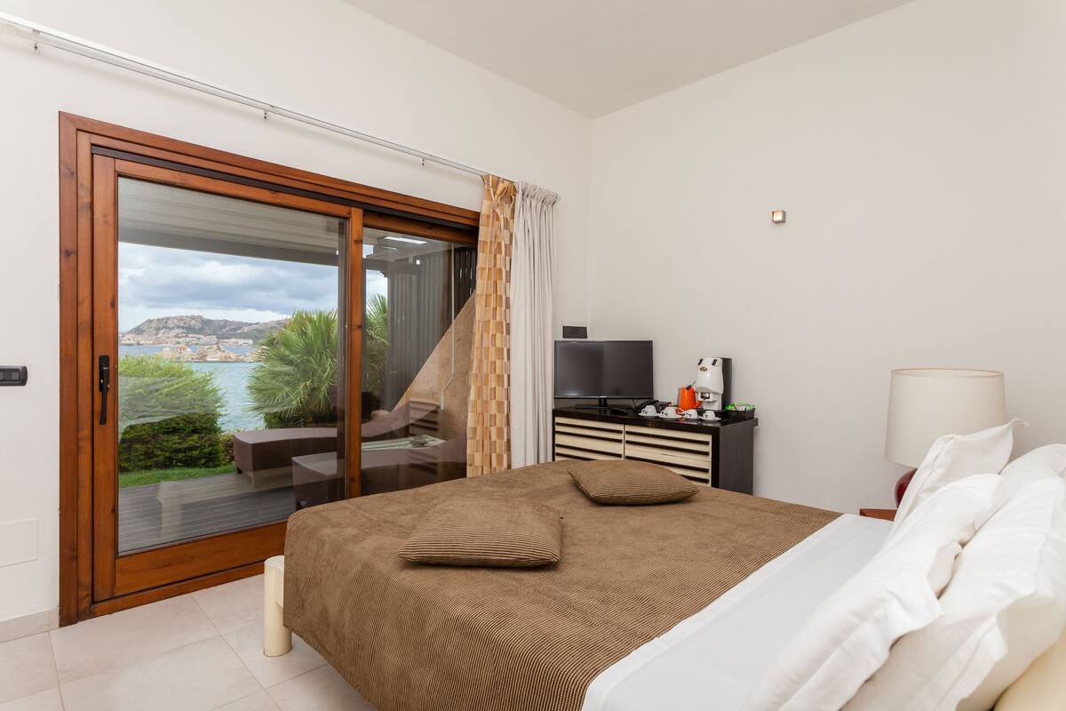A bedroom with a large bed, a TV, a lamp, and a view of the outdoors.
