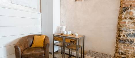 Una habitación acogedora con un sofá de cuero, una pequeña mesa de madera con una cafetera y una pared de ladrillo con un cartel 'BONHEUR'.
