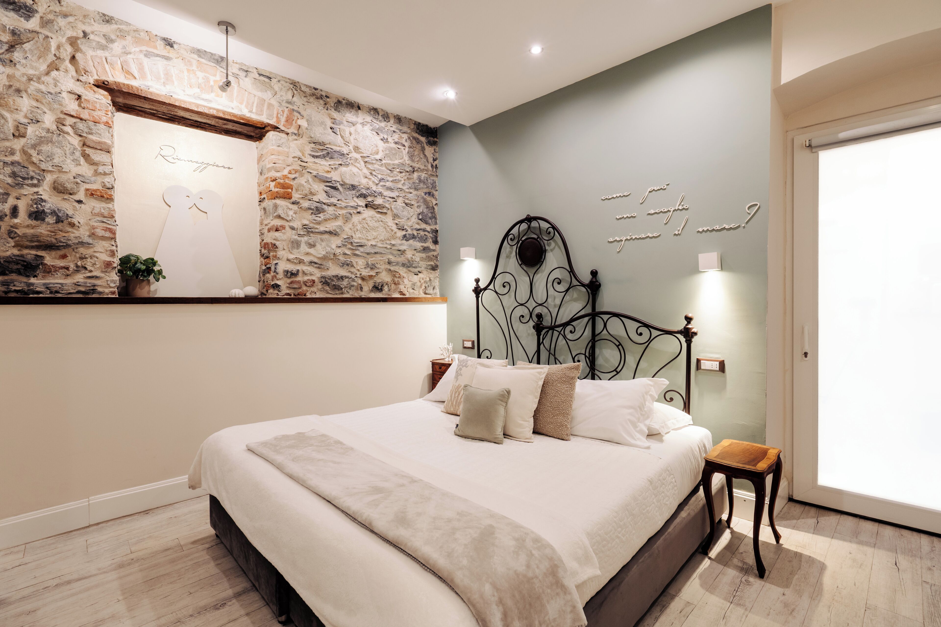 Ein Schlafzimmer mit einer Steinwand, einem Bett mit weißer Bettwäsche, einem Zierteil am Kopfteil und einem kleinen Holzschemel.