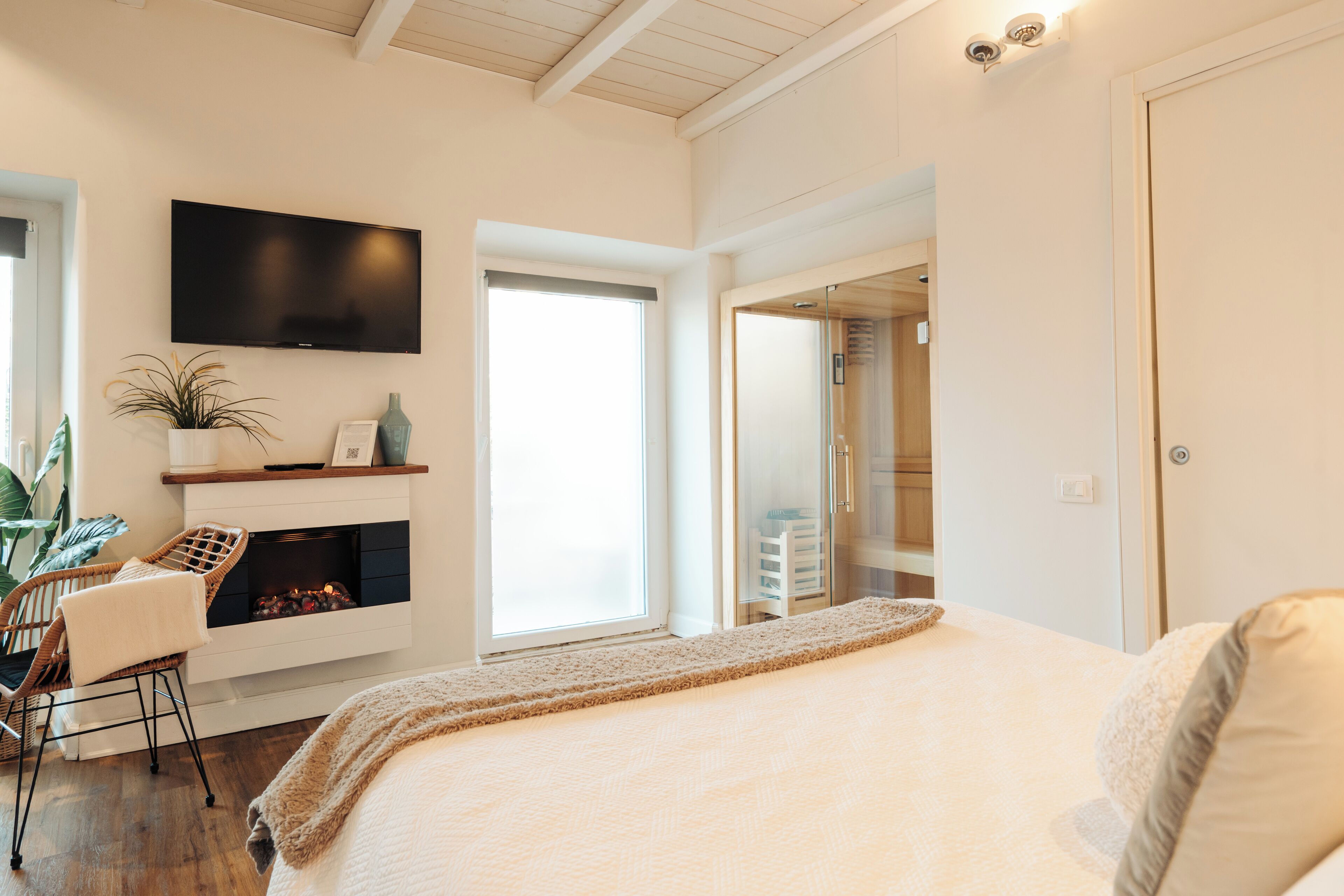 Un dormitorio con una cama grande, chimenea, televisor montado en la pared y ventana que proporciona luz natural.