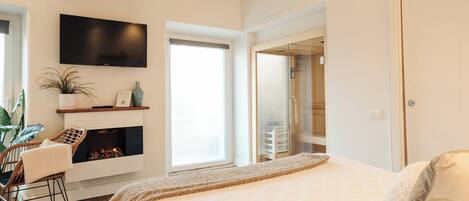 Un dormitorio con una cama grande, chimenea, televisor montado en la pared y ventana que proporciona luz natural.