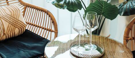 A wicker chair with a black cushion, a glass table with a decorative plate, and a large leafy plant.