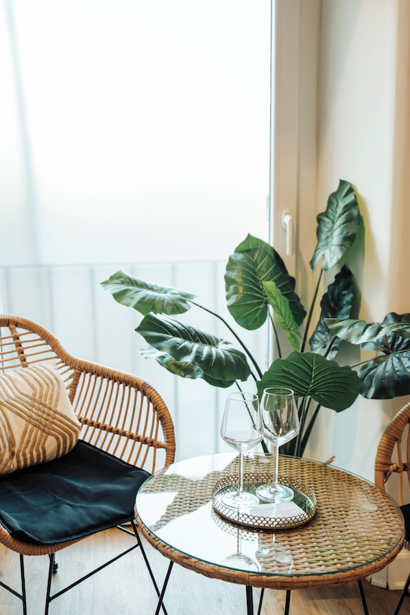 A wicker chair with a black cushion, a glass table with a decorative plate, and a large leafy plant.