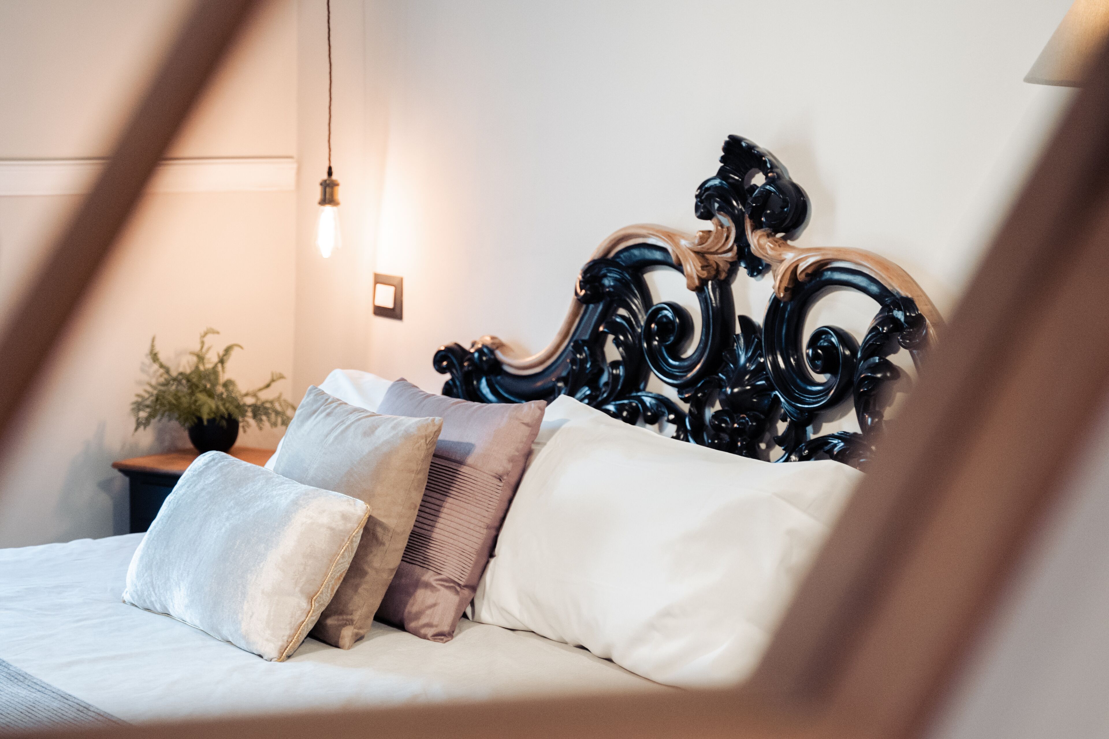 A bed with a dark headboard, multiple pillows, and a bedside table with a lamp.