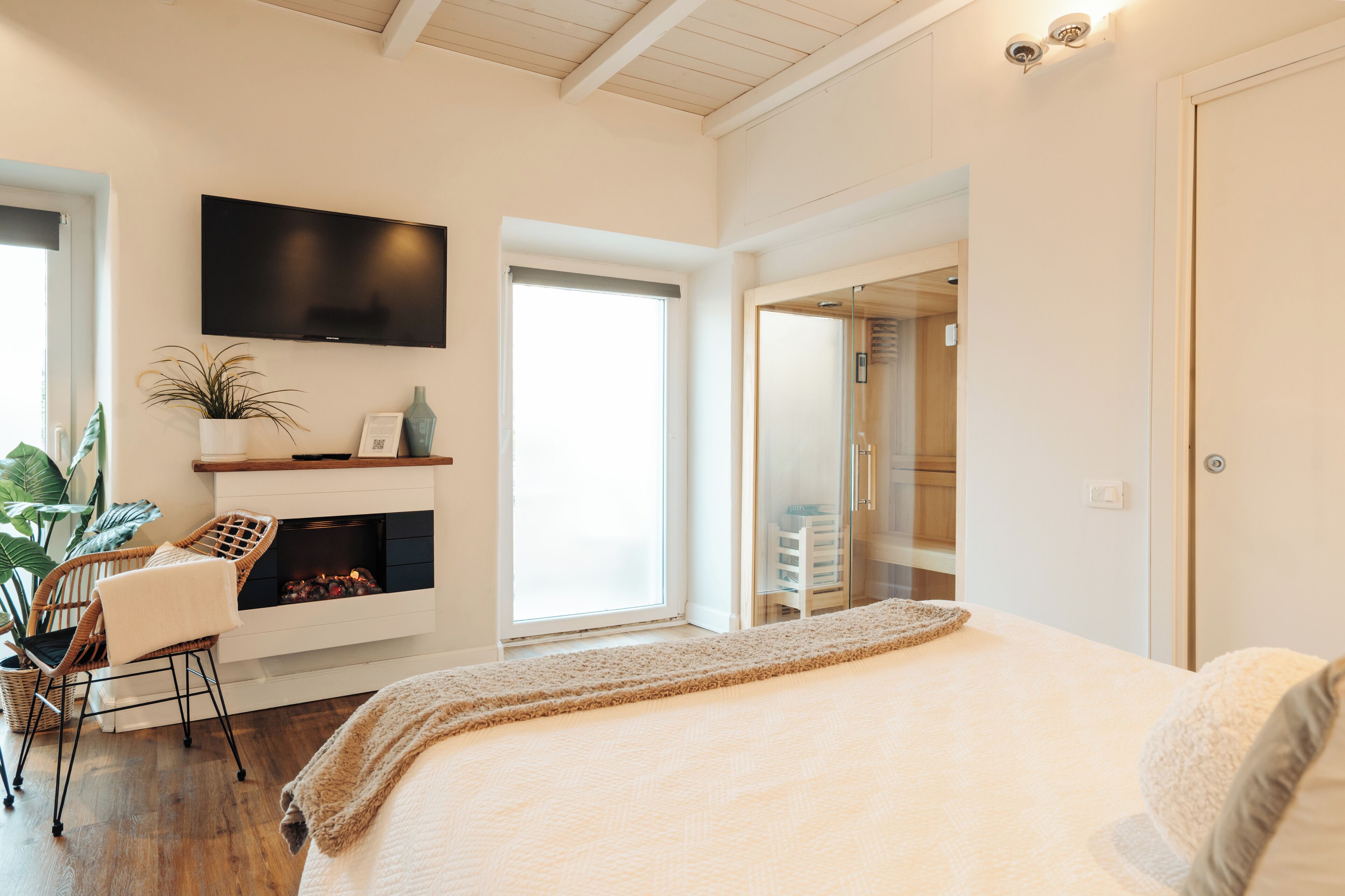 A modern bedroom with a large bed, a fireplace, a TV, and a view of the outside.